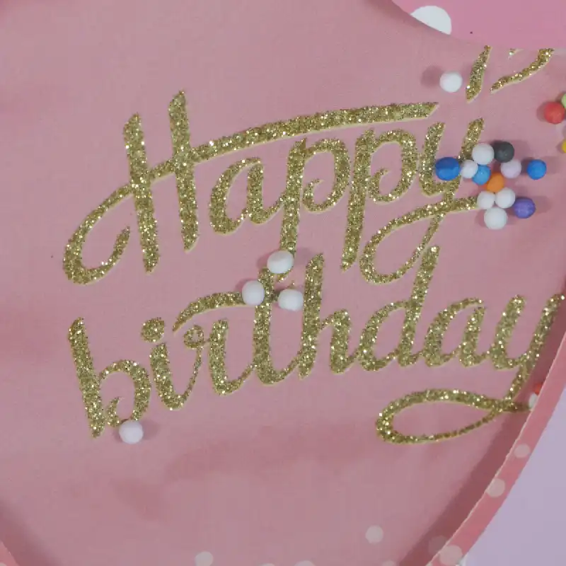 Detale aplikacji 3D w kształcie balonu na torebce. Złoty, brokatowy napis Happy Birthday oraz dekoracyjne, drobne kuleczki na różowym tle.