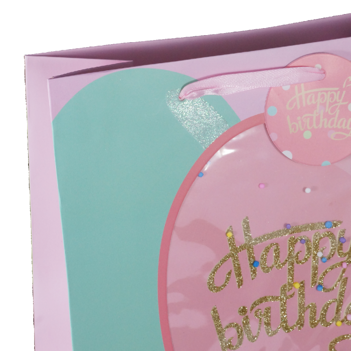 Zbliżenie na górną część torebki prezentowej z różową wstążką jako uchwytem i ozdobną zawieszką z napisem Happy Birthday.