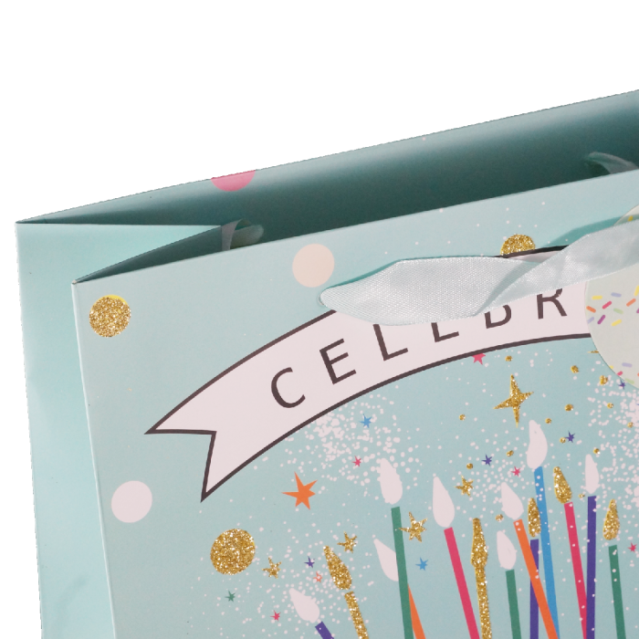Zbliżenie na górną część torebki z napisem Celebrate, brokatowymi detalami oraz wstążkowym uchwytem.
