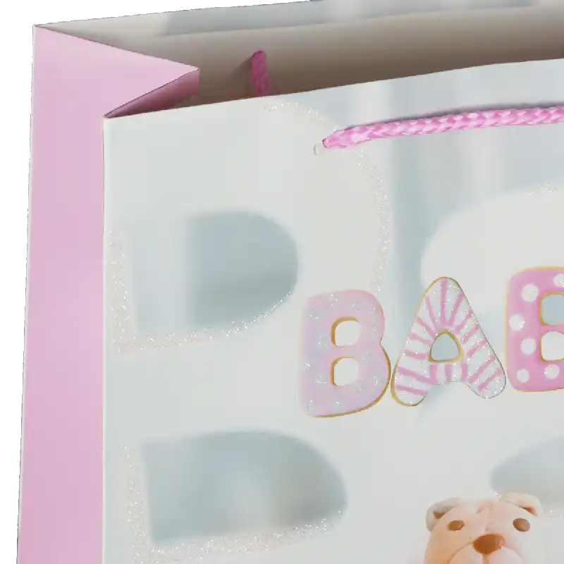 Fragmentaryczne ujęcie górnej części torebki prezentowej, koncentrujące się na detalach napisu oraz strukturze papieru z brokatowymi akcentami.