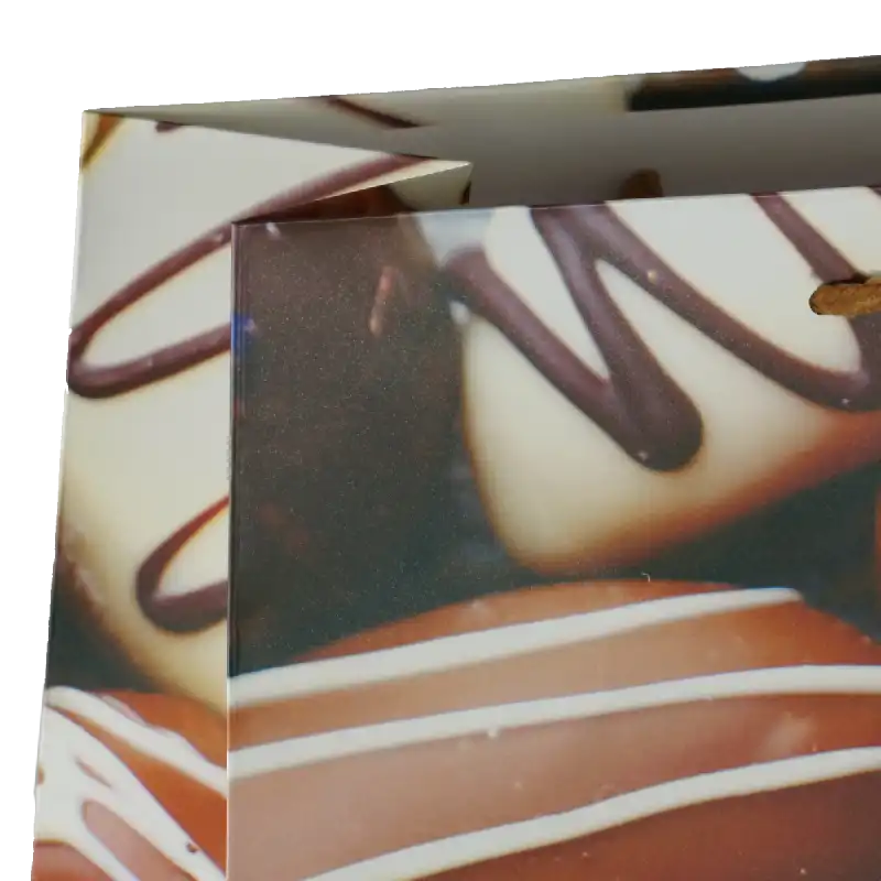Zbliżenie na górną krawędź torebki prezentowej z nadrukiem czekoladek. Widoczne miejsce na uchwyty oraz detale grafiki.