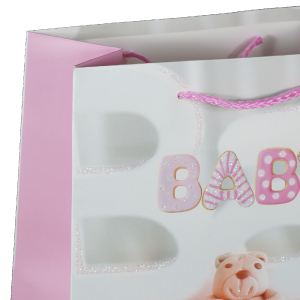 Zbliżenie na górną część różowej torebki prezentowej z tasiemkami i ozdobnym nadrukiem literowym BABY.