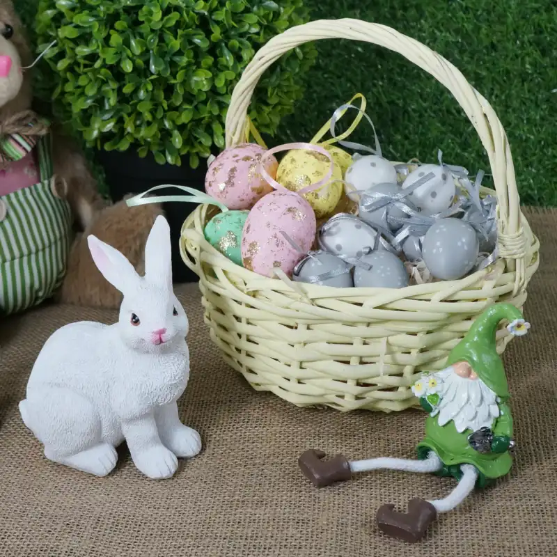 Żółty kosz wiklinowy 22 cm wypełniony wielkanocnymi jajkami, ustawiony obok ceramicznego zająca i figurki krasnala na stole.