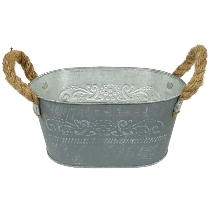 Owalna metalowa osłonka o długości 18 cm w kolorze szarym. Posiada postarzany styl, ozdobne wytłaczane wzory roślinne oraz dwa praktyczne uchwyty z jutowego sznura.