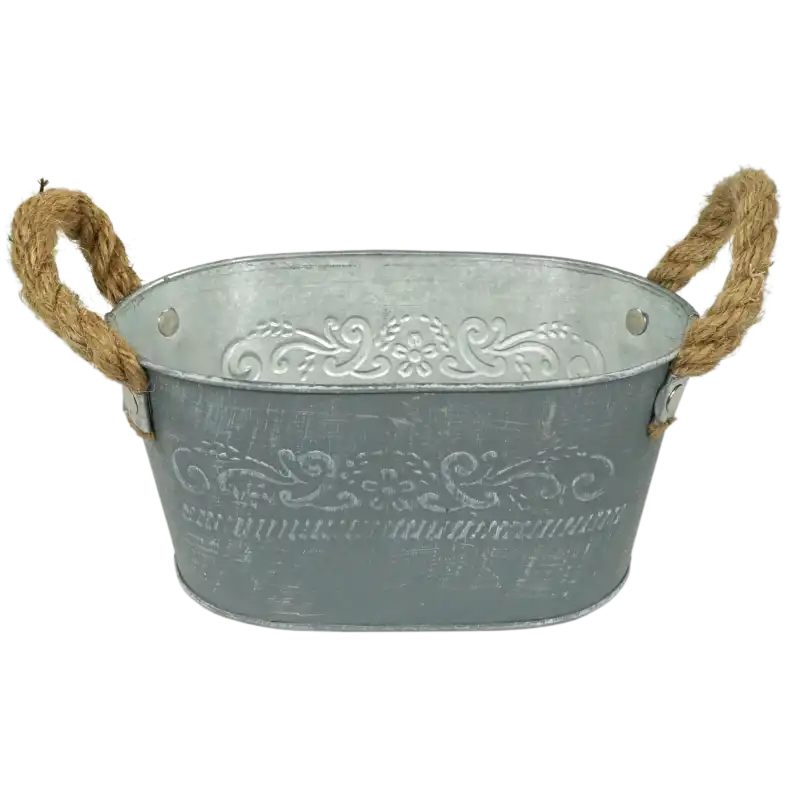 Owalna metalowa osłonka o długości 18 cm w kolorze szarym. Posiada postarzany styl, ozdobne wytłaczane wzory roślinne oraz dwa praktyczne uchwyty z jutowego sznura.