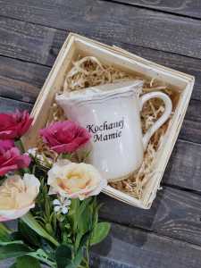Ceramiczny kubek Kochanej Mamie o wysokości 11 cm w ozdobnym koszu z łuby z wełną drzewną i kwiatami. Stylowy zestaw upominkowy.