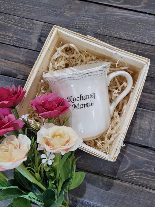 Ceramiczny kubek Kochanej Mamie o wysokości 11 cm w ozdobnym koszu z łuby z wełną drzewną i kwiatami. Stylowy zestaw upominkowy.