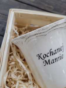 Detaliczna fotografia postarzanego rantu ceramicznego kubka z dedykacją Kochanej Mamie, umieszczonego w koszyku z wełną.