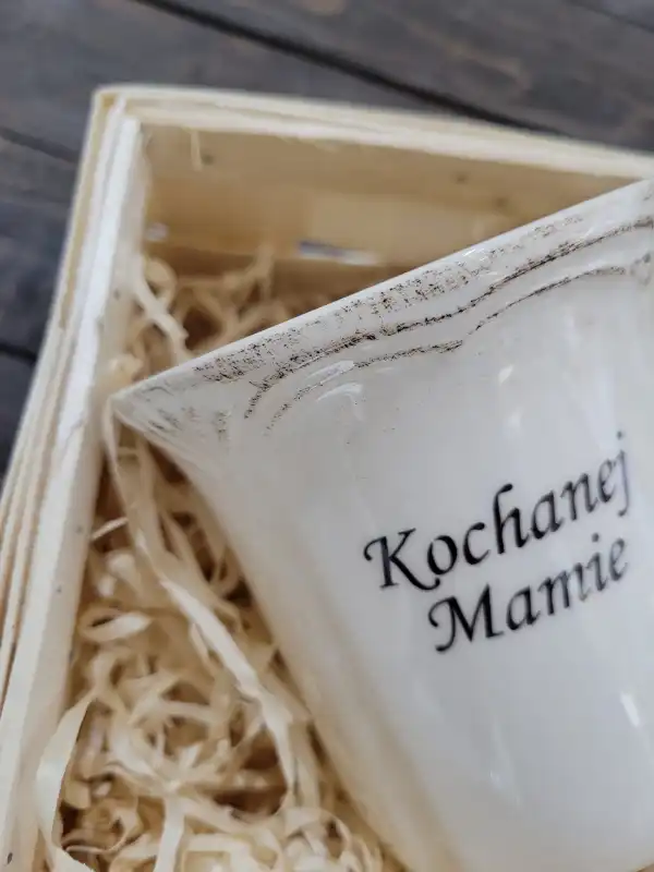 Detaliczna fotografia postarzanego rantu ceramicznego kubka z dedykacją Kochanej Mamie, umieszczonego w koszyku z wełną.