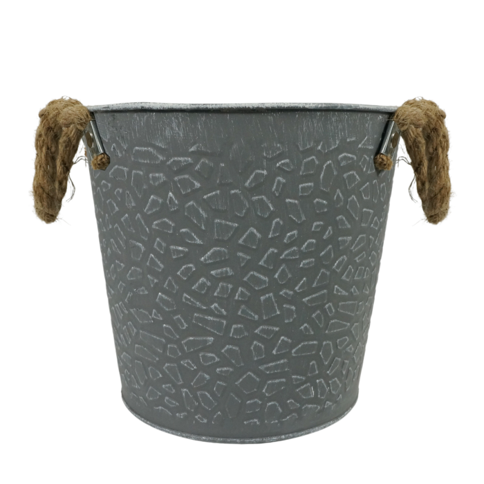 Metalowa osłonka szara o średnicy 18 cm. Dekoracyjna doniczka w postarzanym stylu posiada tłoczony wzór na bokach oraz praktyczne uchwyty wykonane z jutowego sznura.
