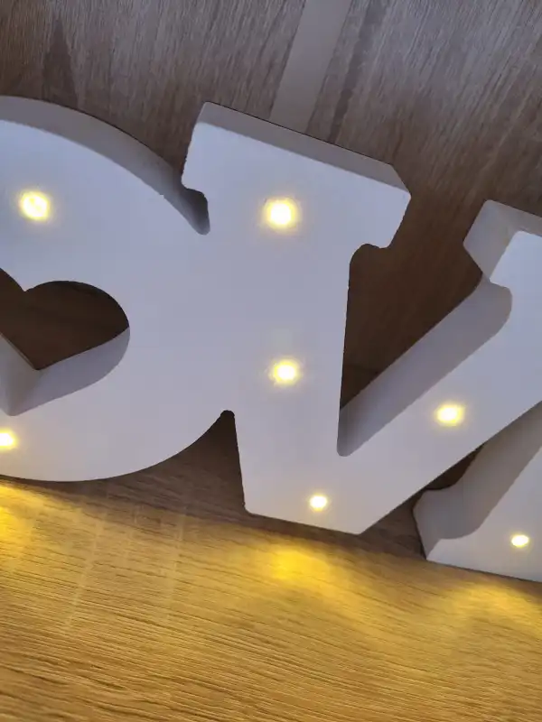 Fragment białego napisu LOVE o długości 44 cm z wyraźnym zarysem liter. Ciepłe światło LED subtelnie rozświetla drewnianą strukturę dekoracji, podkreślając jej biały kolor.