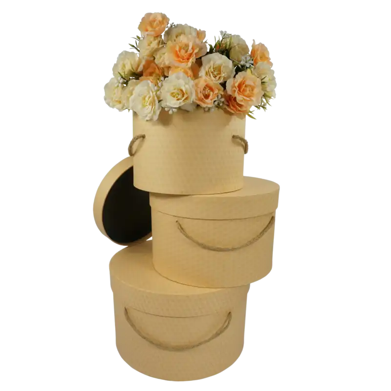 Zestaw 3 flowerboxów kraft z pokrywkami i uchwytami ze sznura wypełnionych sztucznymi kwiatami w odcieniach pomarańczy.