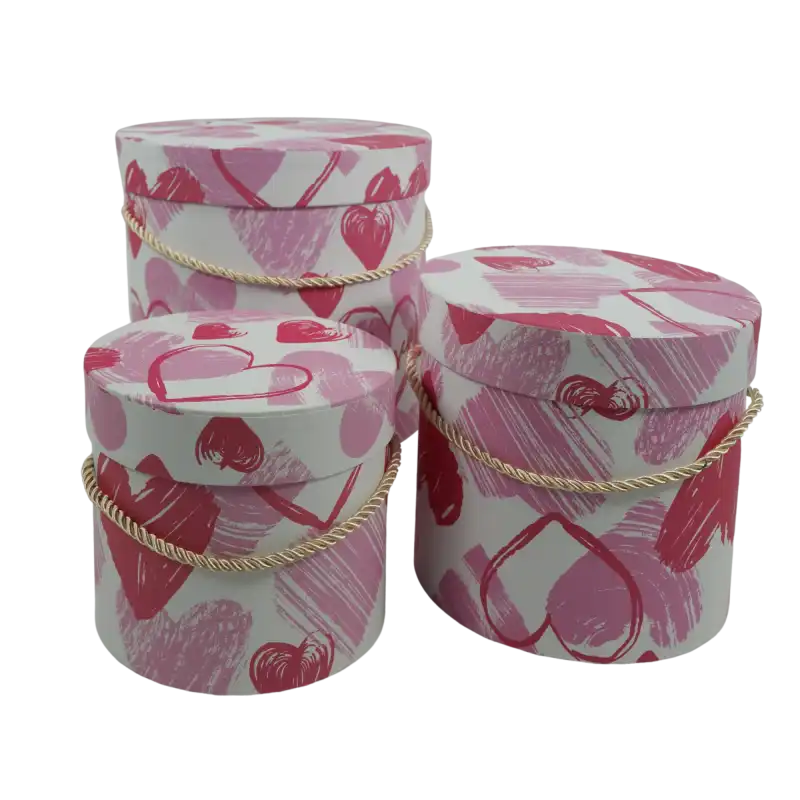 Zestaw trzech okrągłych flowerboxów o wysokości 12 cm, 15 cm i 17 cm. Pudełka ze wzmacnianego papieru z nadrukiem w serca posiadają sznurkowe uchwyty i pokrywki.
