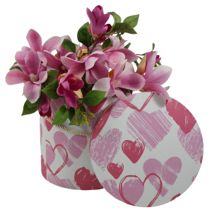Aranżacja flowerboxa wypełnionego kwiatami magnolii. Obok pudełka znajduje się jego pokrywka z wyraźnym wzorem serc, prezentująca funkcjonalność kompletu.