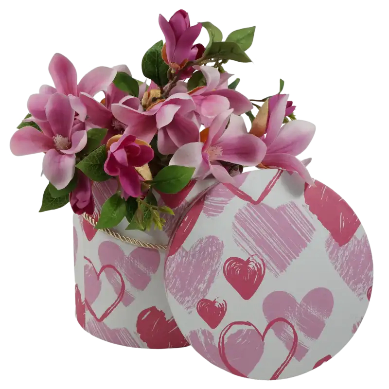 Aranżacja flowerboxa wypełnionego kwiatami magnolii. Obok pudełka znajduje się jego pokrywka z wyraźnym wzorem serc, prezentująca funkcjonalność kompletu.