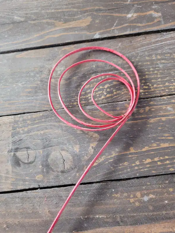 Zbliżenie na spiralnie zwiniętą część różowej sprężynki rattanowej, ułożonej na ciemnym, drewnianym podłożu, podkreślające fakturę materiału.