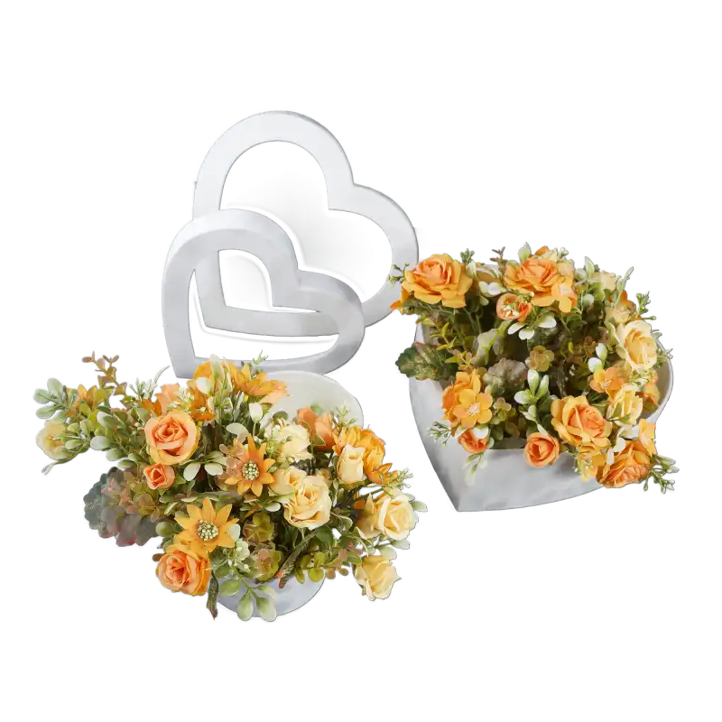 Dwa welurowe flowerboxy w kształcie serc wypełnione sztucznymi kwiatami w odcieniach pomarańczu. Ujęcie z boku prezentuje estetykę wykonania pudełek oraz ich praktyczne zastosowanie w dekoracji.