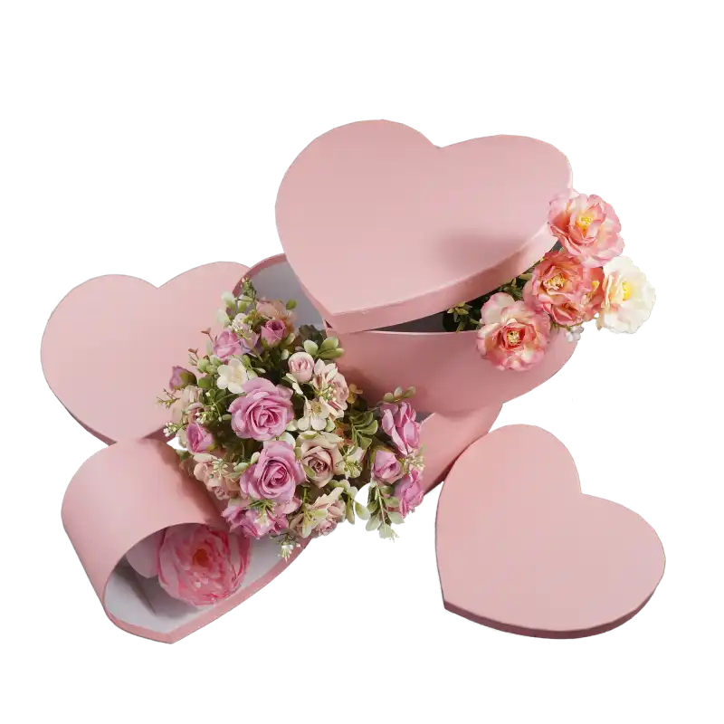Zbiór trzech różowych flowerboxów w kształcie serca z bukietami kwiatów. Jedno pudełko jest puste z położoną obok pokrywką.