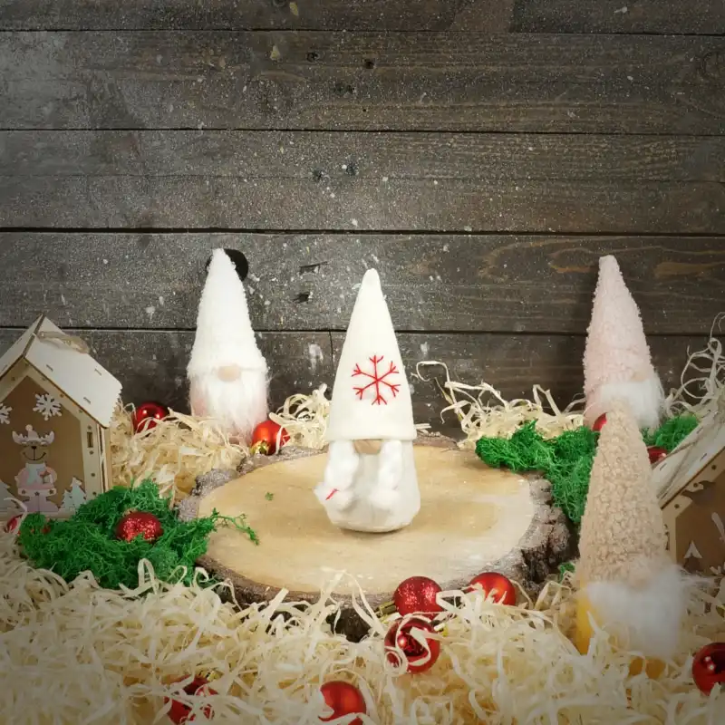 Figurka filcowego skrzata Ewa wyeksponowana na drewnianym plastrze w otoczeniu świątecznych ozdób. Sceneria podkreśla zimowy klimat dekoracji, tworząc harmonijną kompozycję na stole lub kominku.