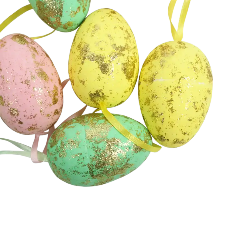 Widok na detale powierzchni pisanek. Wiosenne zawieszki wielkanocne w pastelowych barwach, bogato zdobione połyskującym złotym brokatem. Lekkie styropianowe jajka o wysokości 6 cm z kolorowymi tasiemkami.