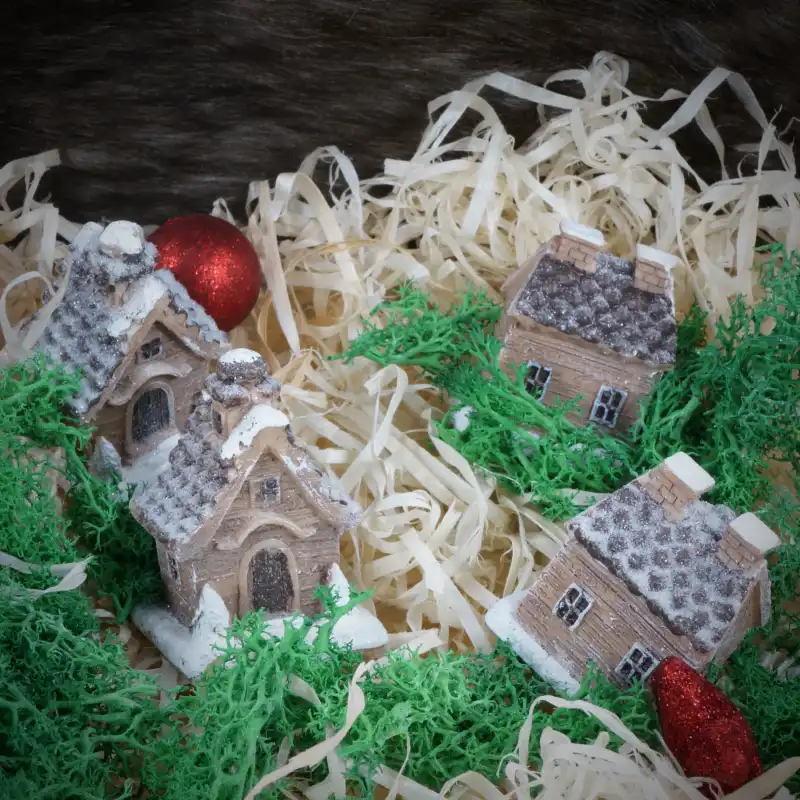 Aranżacja czterech miniaturowych domków umieszczonych wśród zielonego mchu i ozdobnych wypełniaczy, tworząca zimowy klimat.