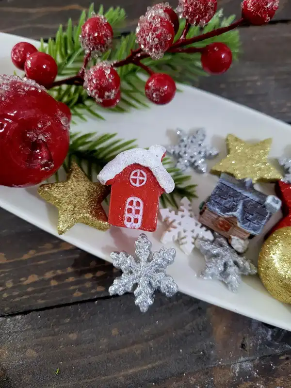 Aranżacja świąteczna na białym talerzu z czerwoną gałązką, miniaturowymi domkami oraz brokatowymi śnieżynkami w odcieniach bieli i srebra.
