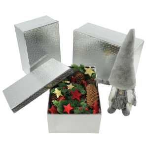 Srebrny flowerbox wypełniony świątecznymi gałązkami i szyszkami obok ozdobnej figurki skrzata.