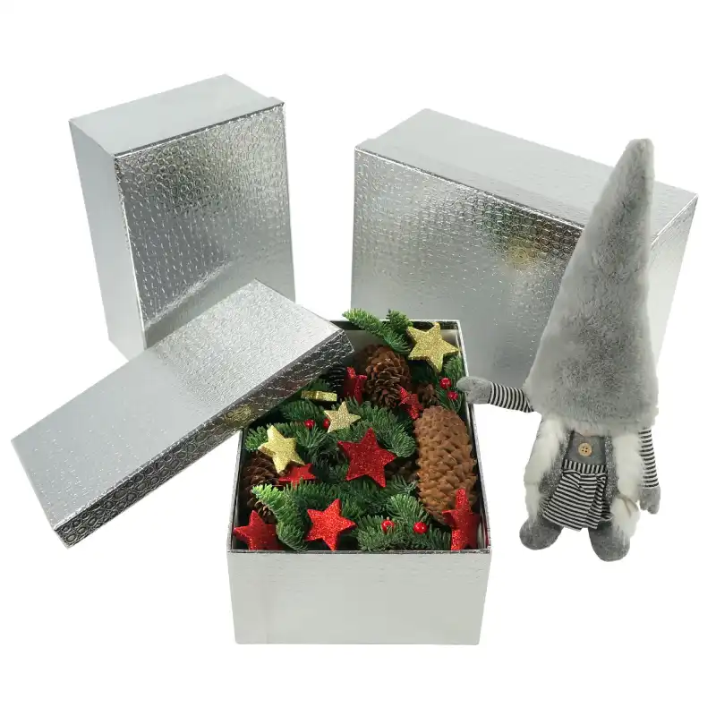 Srebrny flowerbox wypełniony świątecznymi gałązkami i szyszkami obok ozdobnej figurki skrzata.
