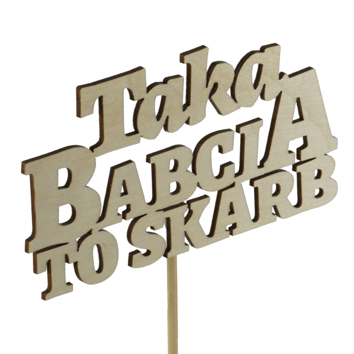 Zbliżenie na drewniany napis Taka babcia to skarb umieszczony na długim patyczku. Dekoracja pokazana pod kątem, podkreślającym fakturę naturalnego drewna i precyzyjne wycięcie liter.