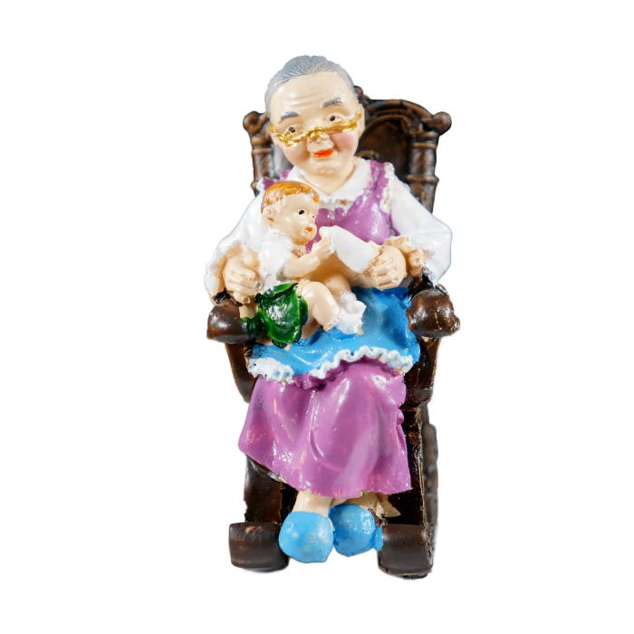 Figurka Babcia w fotelu o wysokości 10 cm wykonana z tworzywa. Przedstawia babcię karmiącą dziecko butelką w antycznym fotelu bujanym.