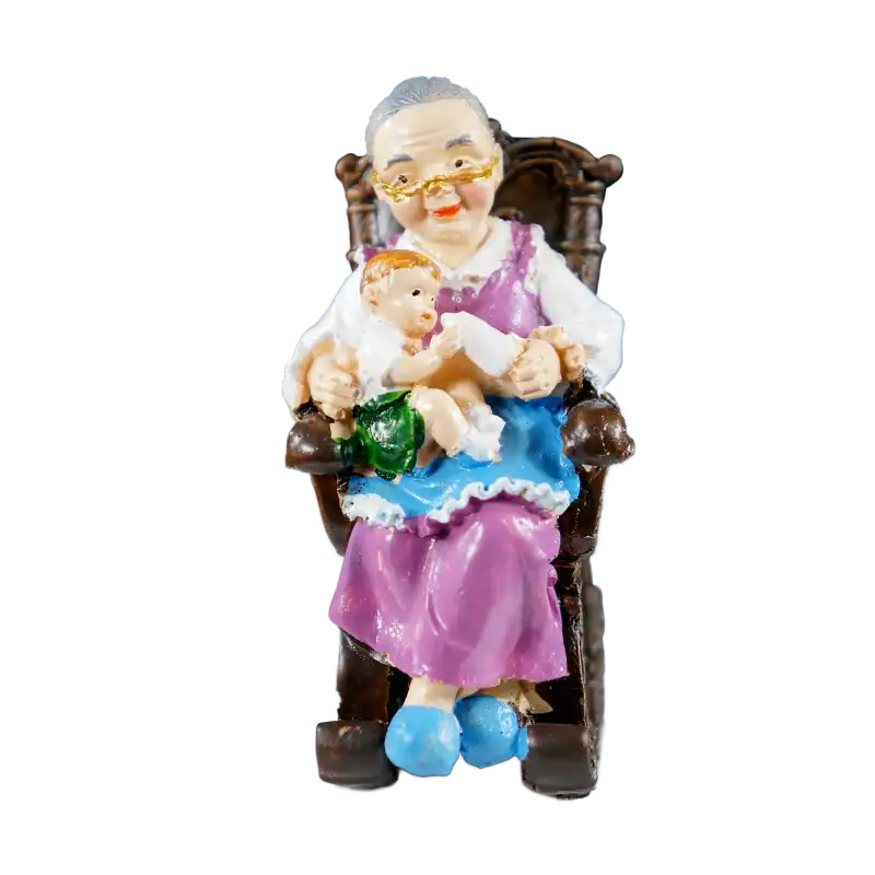 Figurka Babcia w fotelu o wysokości 10 cm wykonana z tworzywa. Przedstawia babcię karmiącą dziecko butelką w antycznym fotelu bujanym.
