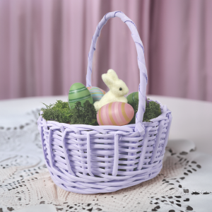 Aranżacja wielkanocna w fioletowym koszyku wiklinowym, ustawiona na białej serwecie, widok z profilu.