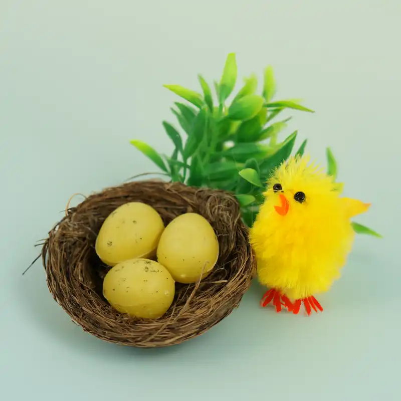 Kompozycja wielkanocna z miękkim kurczaczkiem 4 cm, gniazdkiem z pisankami oraz sztuczną zielenią w tle.