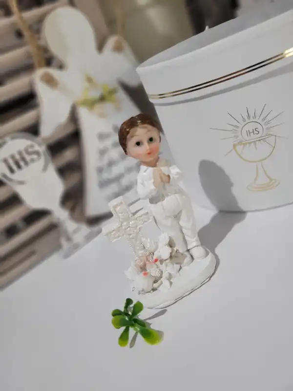 Figurka komunijna chłopca ustawiona obok ozdobnego pudełka z motywem IHS, idealna jako pamiątka uroczystości.