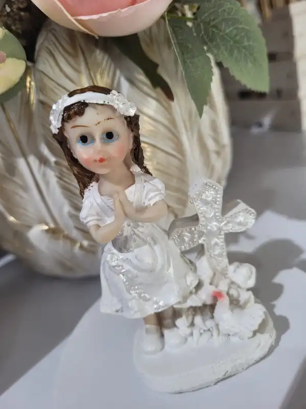 Figurka komunijna dziewczynki 10 cm na tle jasnych kwiatów, ukazująca delikatne zdobienia stroju.