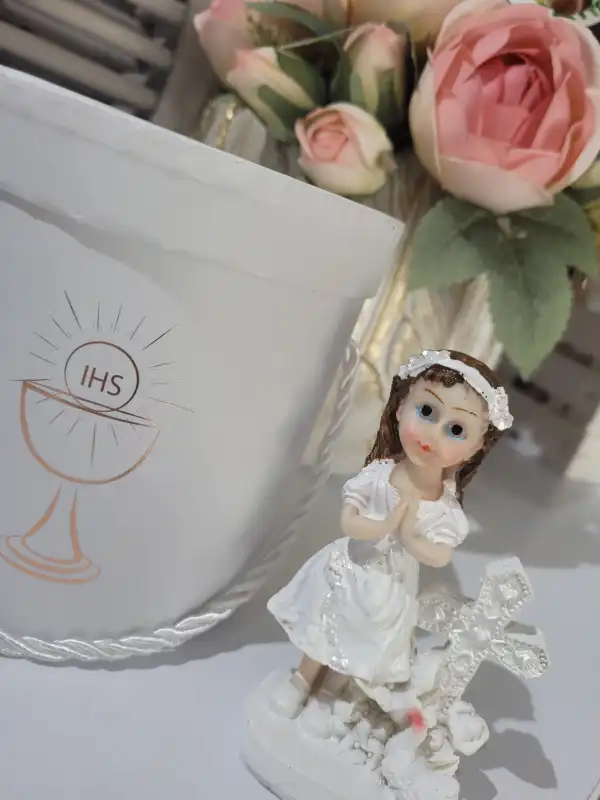 Figurka komunijna dziewczynki 10 cm ustawiona obok pamiątkowego pudełka z motywem IHS i kwiatów.