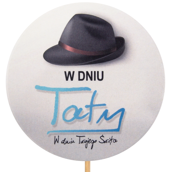 Zbliżenie na okrągły topper W Dniu Taty o średnicy 9 cm. Grafika przedstawia czarny kapelusz i niebieski napis na jasnym tle. Element dekoracyjny na długim piku.