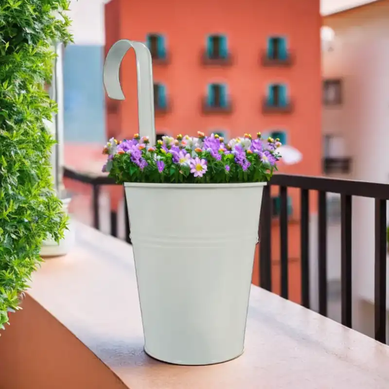 Biała metalowa osłonka z uchwytem o średnicy 12 cm z kwiatową kompozycją, przeznaczona do zawieszenia na balustradzie balkonu.