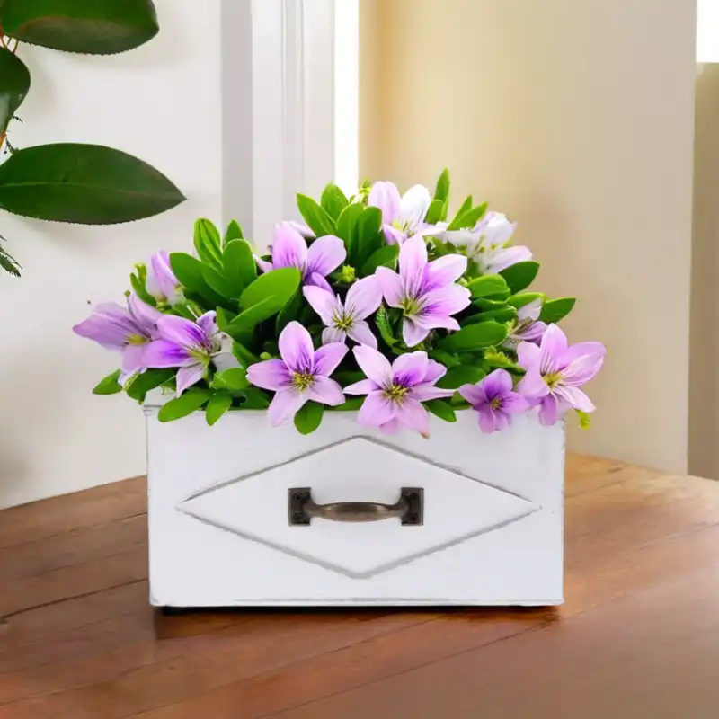 Biała osłonka szuflada 23x13 cm z dekoracyjną metalową rączką i wypełniona kolorową kompozycją kwiatową na drewnianym blacie.