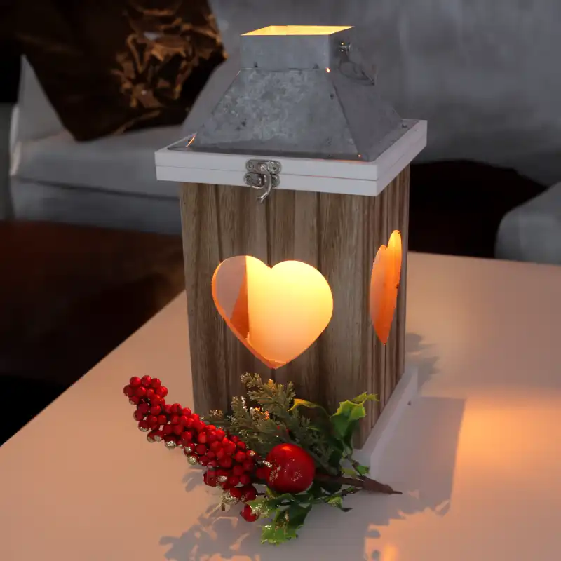 Lampion w aranżacji z dekoracją świąteczną, emitujący ciepłe światło przez wycięte w drewnie serca.