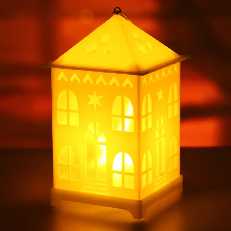 Zbliżenie na lampion LED w kształcie domku, który rozświetla ciemne tło ciepłym blaskiem, podkreślając przytulny charakter tej dekoracji.