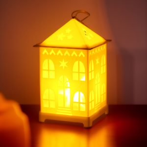 Klimatyczny lampion LED domek z włączonym oświetleniem wewnątrz, tworzącym ciepłe refleksy świetlne w ciemniejszym otoczeniu.