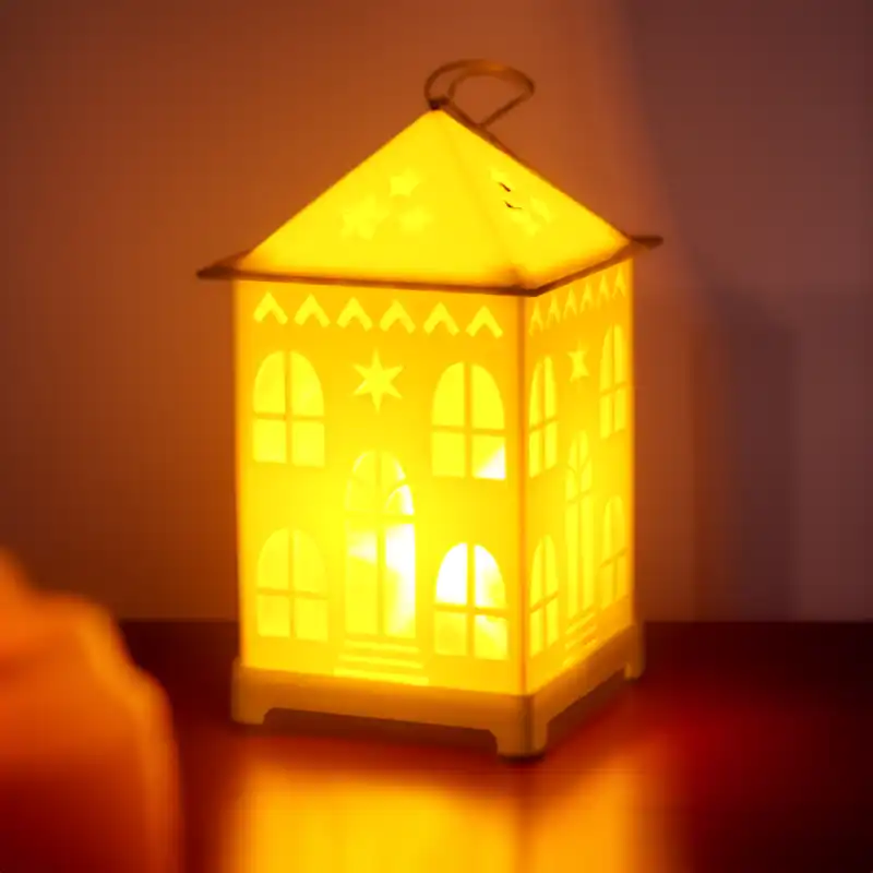 Klimatyczny lampion LED domek z włączonym oświetleniem wewnątrz, tworzącym ciepłe refleksy świetlne w ciemniejszym otoczeniu.