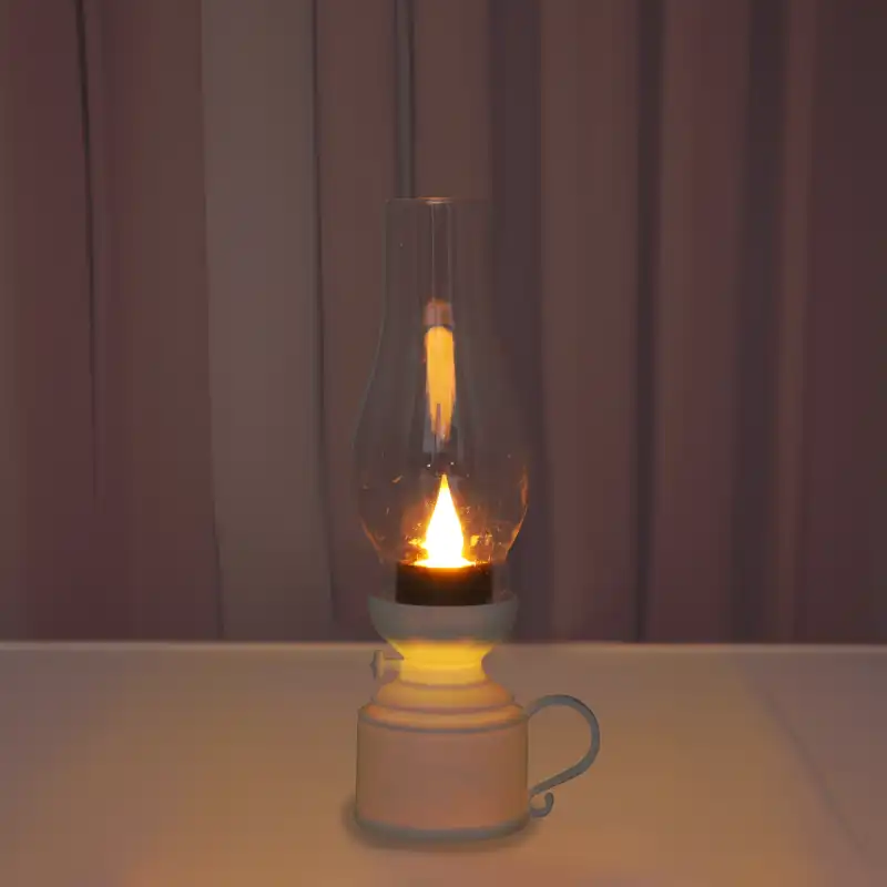 Nastrojowe ujęcie zapalonej lampy naftowej LED na jasnym tle. Urządzenie emituje ciepłe światło, imitujące naturalny blask świecy.