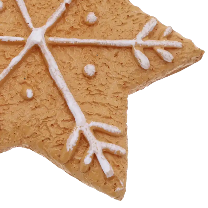 Zbliżenie na fakturę zawieszki przypominającej piernikowe ciastko oraz białe zdobienie w kształcie śnieżynki i kropek.