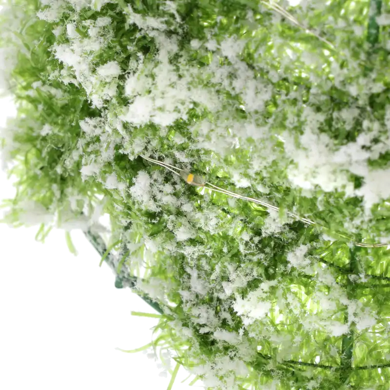 Detail oświetlenia LED wplecionego w ośnieżone, zielone gałązki choinki, podkreślający ciepłą barwę światła oraz strukturę sztucznego śniegu na dekoracji.