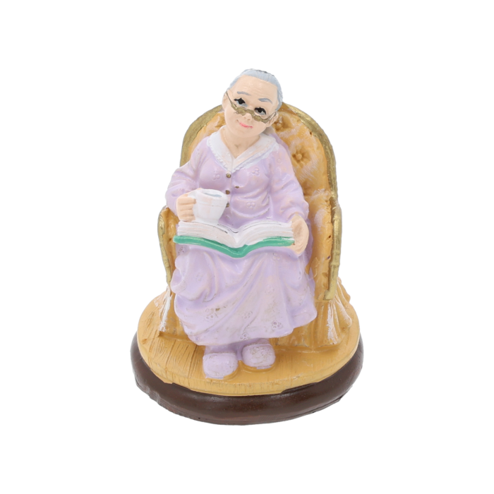 Figurka babcia z filiżanką i książką o wysokości 7 cm w fioletowej sukni, siedząca w fotelu. Detal prezentuje postać w okularach, idealna dekoracja na prezent.
