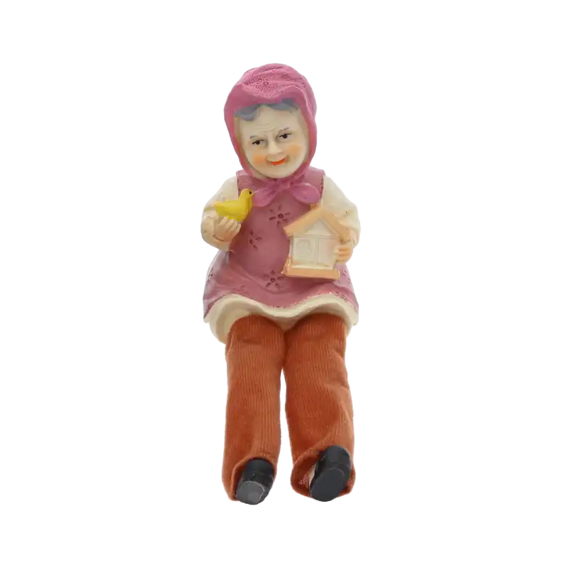Figurka babci o wysokości 11 cm z materiałowymi nogawkami, trzymająca w dłoniach małego ptaszka oraz domek, prezentowana na wprost.