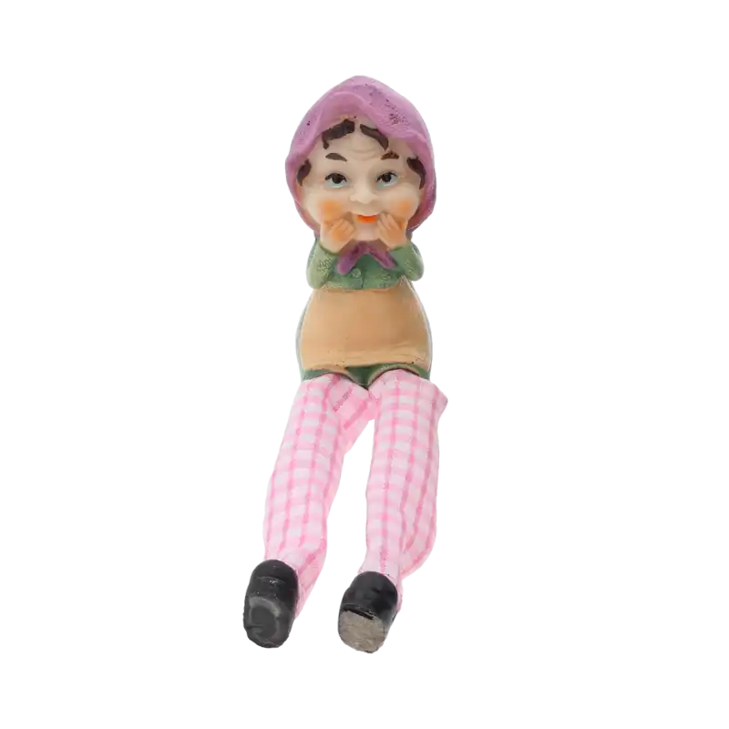 Figurka babci o wysokości 9 cm z luźno opadającymi nogawkami w różową kratkę. Prezentuje uroczy design z tkaniny i tworzywa, idealna jako ozdoba wnętrza.