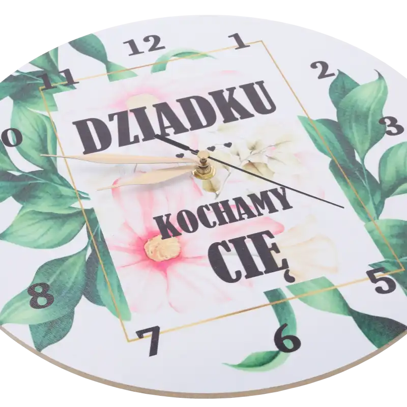 Zbliżenie na tarczę zegara z napisami i motywem roślinnym, pokazujące szczegóły nadruku oraz wskazówki mechanizmu.